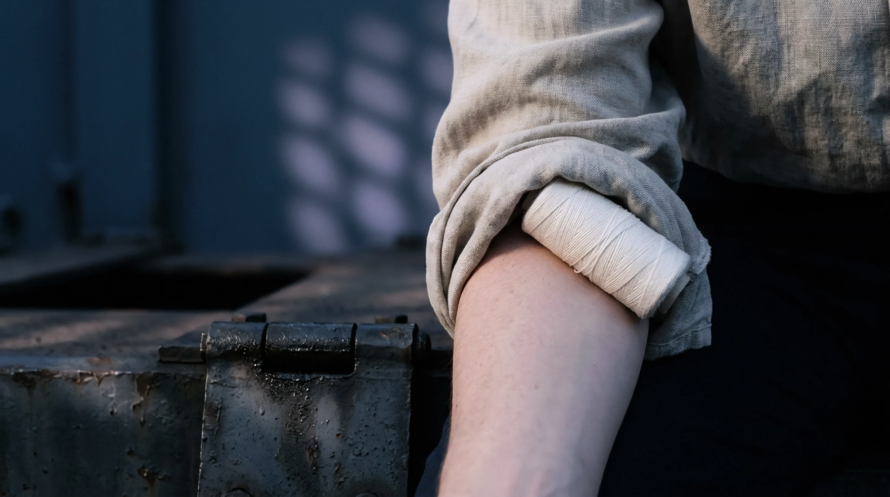A spool of white thread rests securely inside the folded cuff of a linen sleeve on a person at work.